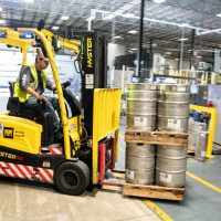 Forklift operator in warehouse moving beer kegs for distribution.
