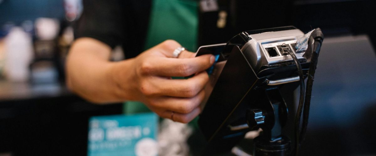Close-up of a barista processing a payment using a card reader in a café setting.
