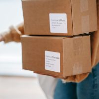 A woman delivering two cardboard boxes to an apartment indoors.