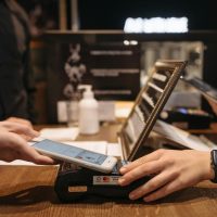 Hands using mobile for contactless payment at café terminal.